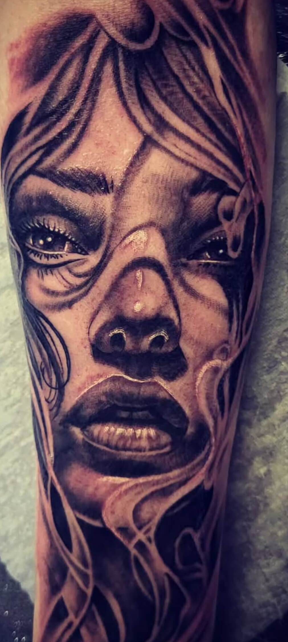Black and grey realism tattoo of a woman's face with intense eyes and abstract flowing line patterns, created at Old Stone Tattoo House in Athlone, Ireland.