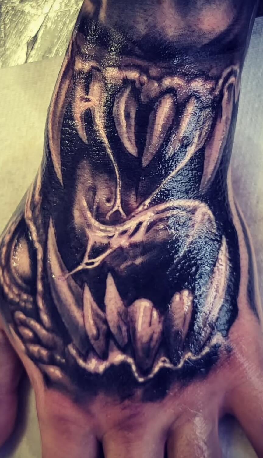 Realistic black and grey tattoo of a monster’s open mouth with sharp fangs and detailed textures, inked on the top of the hand at Old Stone Tattoo House in Athlone, Ireland.