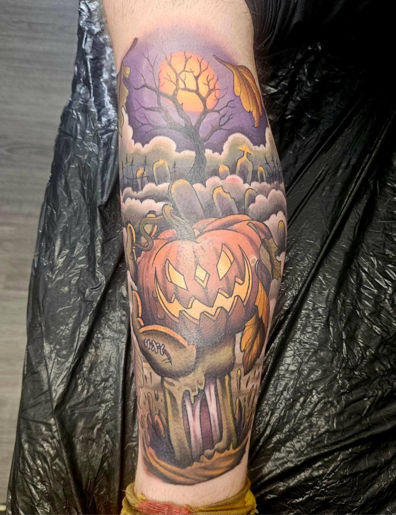 Colorful Halloween-themed tattoo of a grinning jack-o’-lantern-headed creature with a twisted, gnarled stem body, set in a graveyard scene under a purple night sky with a large yellow full moon and a bare tree.