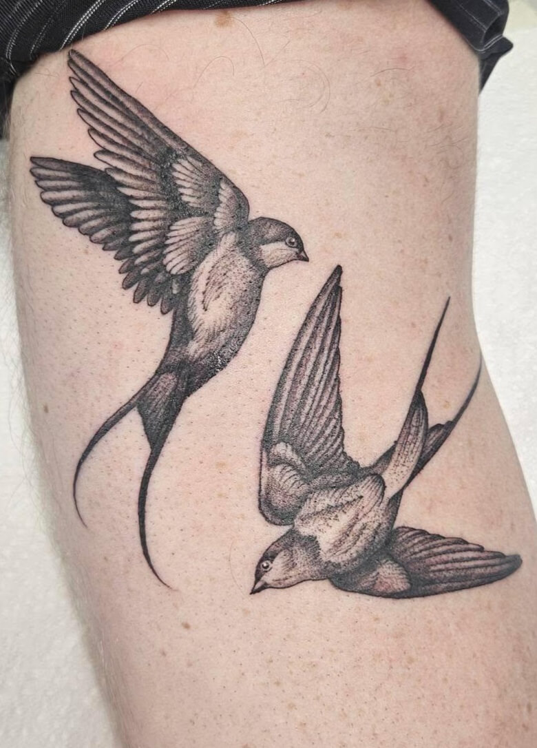 Black and grey tattoo of two swallows in flight, detailed with fine line shading and positioned as if gracefully circling each other